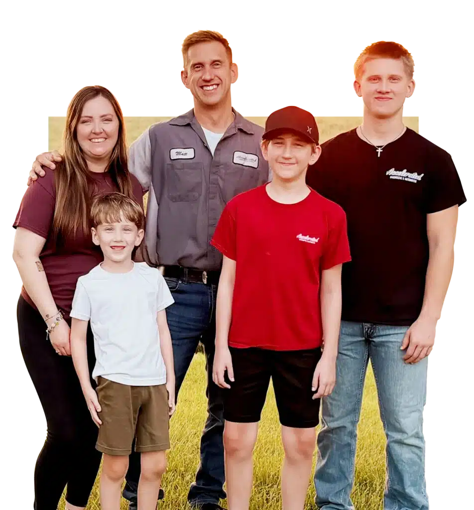 A family of five poses outdoors on grass, smiling. The woman stands to the left, a man in a work shirt stands in the middle, with three boys—two older and one younger—standing in front and beside them.