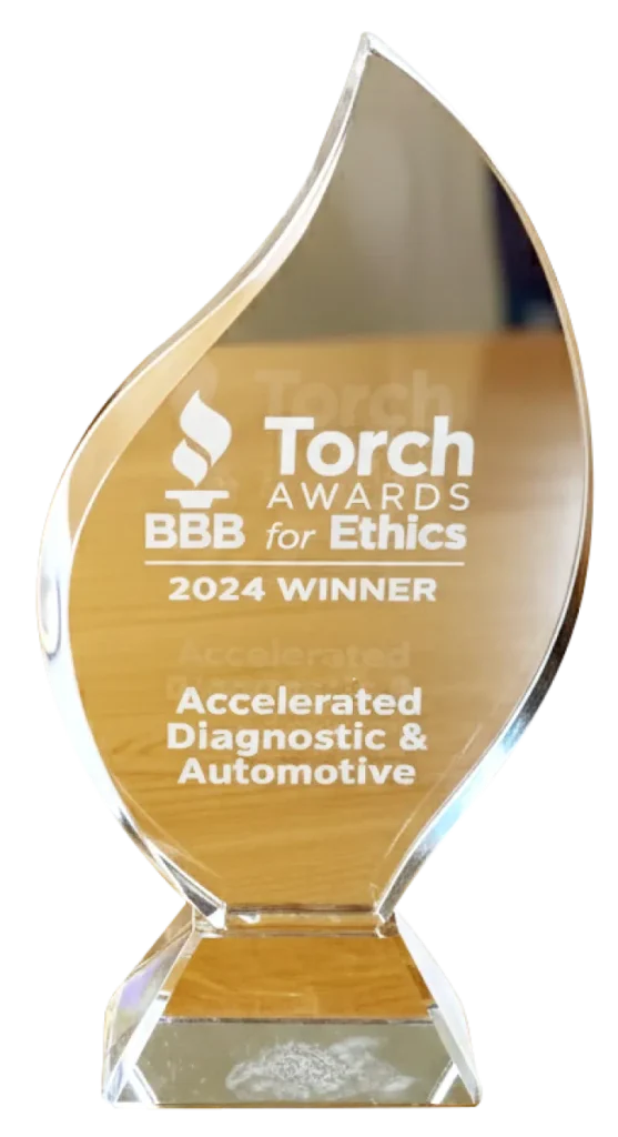 A clear glass award in the shape of a flame reads: Torch Awards for Ethics, BBB, 2024 Winner, Accelerated Diagnostic & Automotive. The award is displayed on a wooden surface.