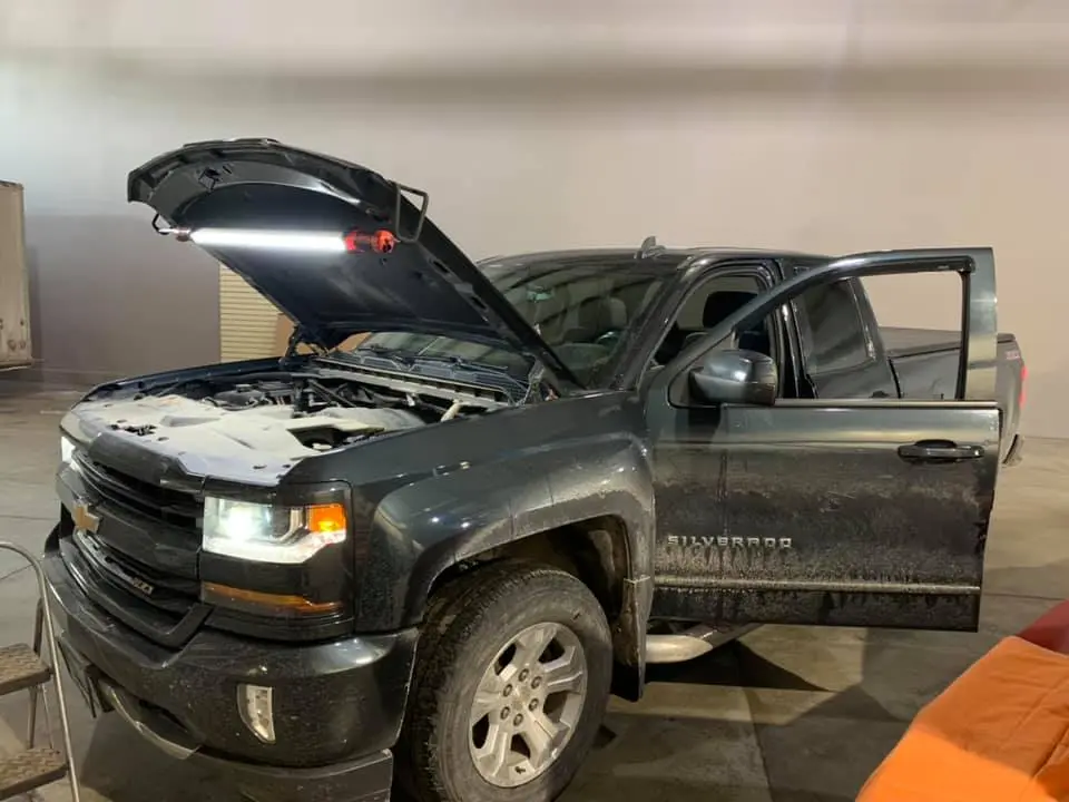 Chevrolet Silverado pickup truck parked indoors with the hood open and a work light illuminating the engine bay, showing the vehicle during inspection or maintenance.