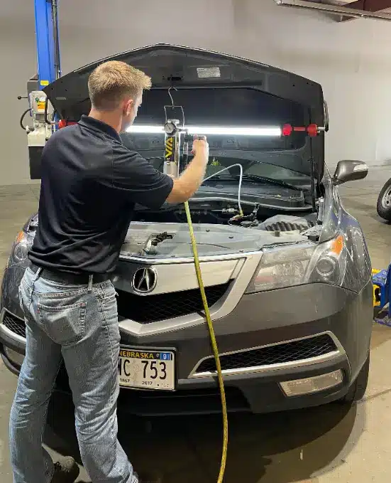 Automotive technician performing engine service on an Acura SUV with the hood open inside a repair shop.