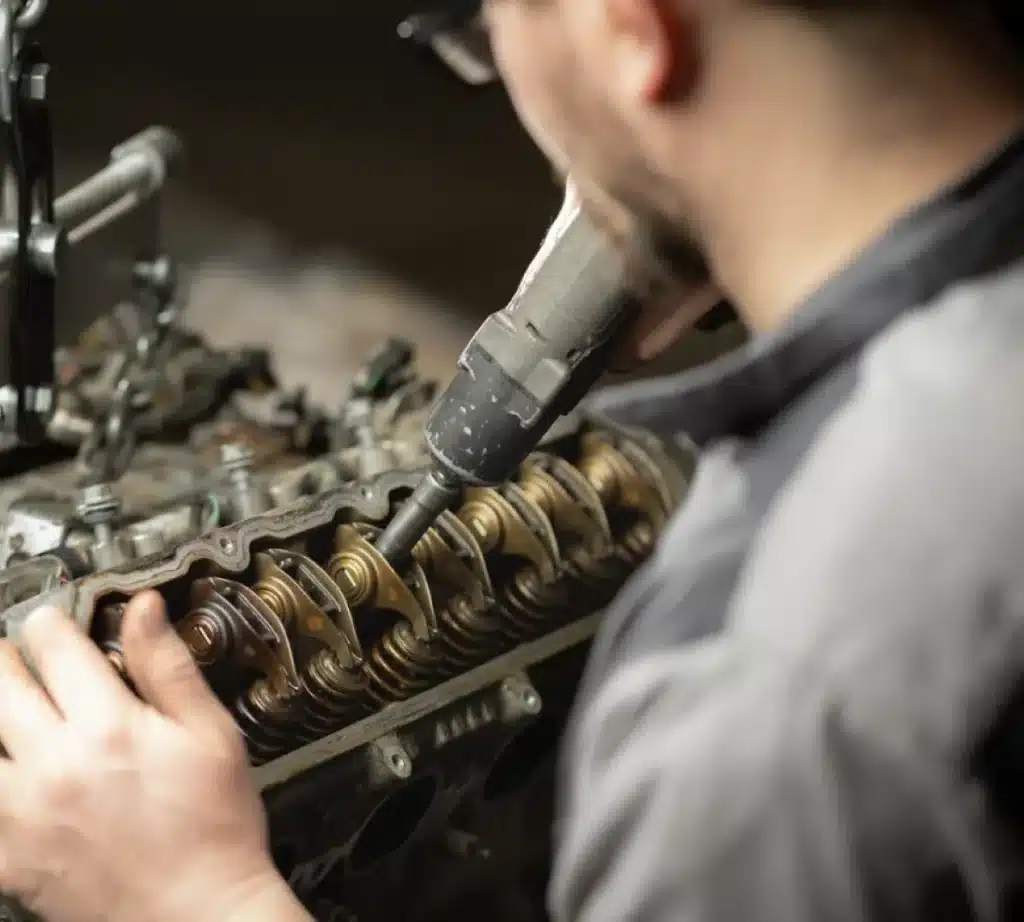 A person using a power tool to work on the exposed valve train of an engine, focusing on mechanical parts and wearing safety glasses and a gray shirt during key fob programming.