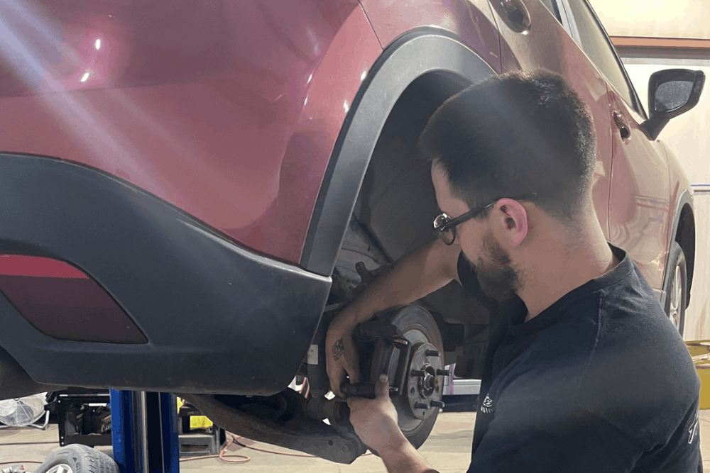 pad slapping, auto repair in Bennington, NE at Accelerated Diagnostic and Automotive. Image of a technician servicing the rear brake assembly on a red SUV with the wheel removed, supporting safe and reliable braking performance.